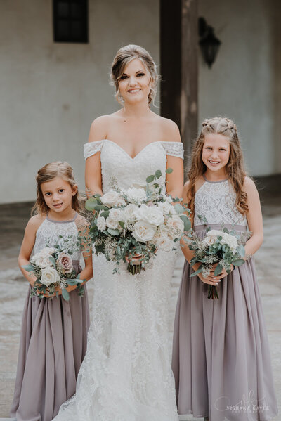 bride standing with flower girls while they all smile