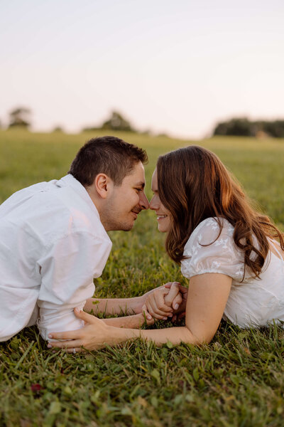 A couple lying in the grass holding hands during their engagement shoot at Waterstone Estates and Farms in Newmarket, Ontario