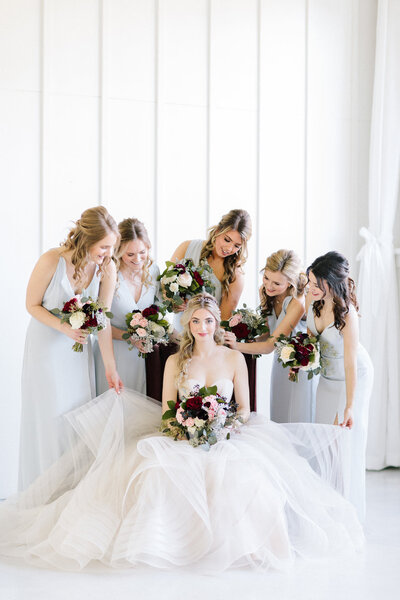 Bride surrounded by bridesmaids holding bouquets and fixing her dress