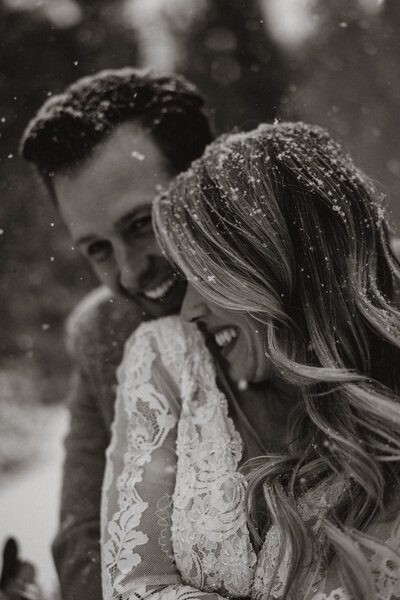 Bride and groom laughing under falling snowflakes, a romantic winter wedding moment in Breckenridge, Colorado.