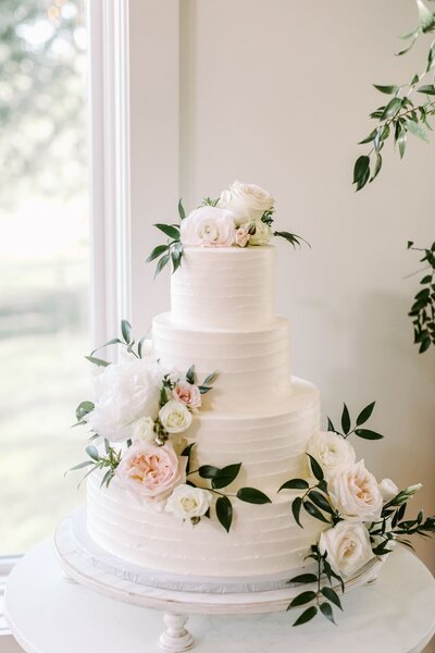 Beautiful wedding cake adorned with fresh floral accents, including blush roses and greenery, styled by Leigh Florist.