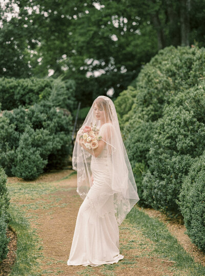 Bride covered in delicate lace veil holds floral bouquet in Cheekwood Gardens in Nashville photographed by Nashville luxury wedding photographer Magnolia Tree Photo Company