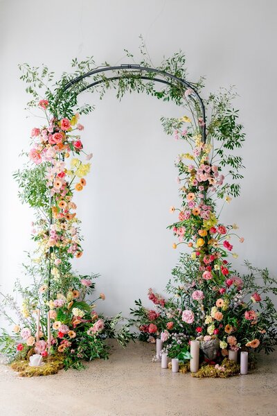 Whimsical floral wedding arch with lush greenery, pastel blooms, and candles at the base, styled by Yours Truly, a wedding planner and designer in New Jersey.