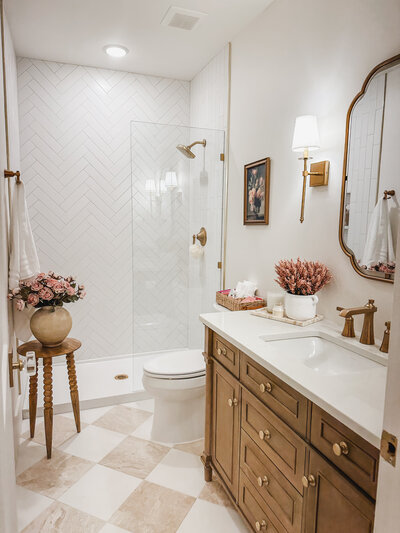 The guest bathroom was elegantly updated with a wood vanity, marble checkered floors and brass fixtures