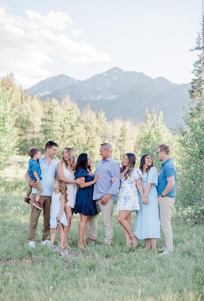 An extended family laughs with each other while standing in a mountain meadow as directed by their Breckenridge Family Photographer