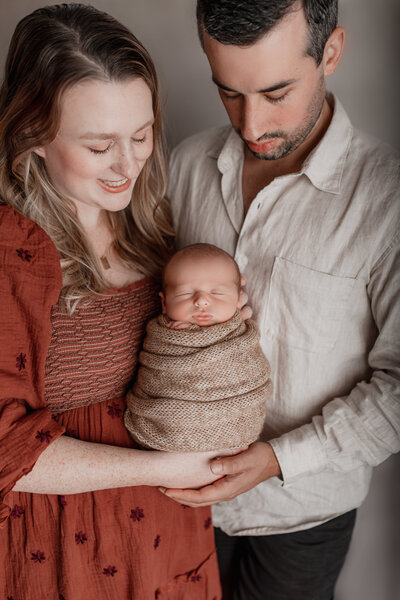 Mom and dad hold baby boy close to their chest in a newborn studio