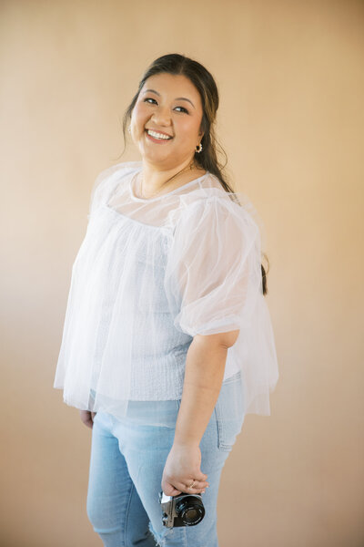 Monique Anne holding a Pentax film camera and smiling in front of a studio background
