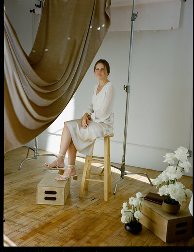 Bailee sitting on a stool in a white dress surrounded by studio equipment