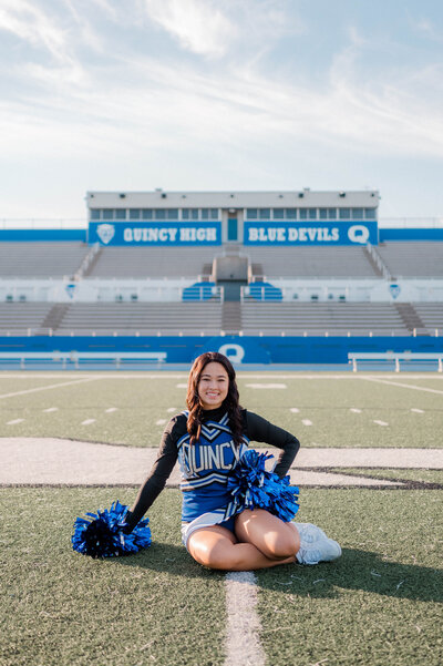 A senior Quincy High School cheerleader poses for the camera in uniform on the football field.