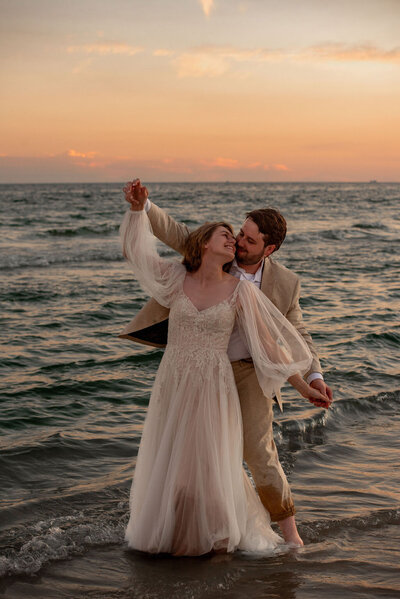 A bride and groom dance in a grassy field with yellow flowers with the Boulder Flatirons in the background.