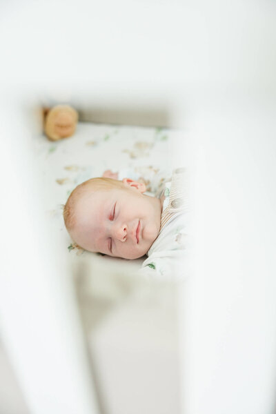 Baby smiling gently in his sleep while sleeping in his cot. Photograph by Julie-Anne Photography