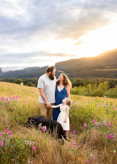 Family of three with black lab smiling and holding hands at sunset in the Columbia River Gorge.