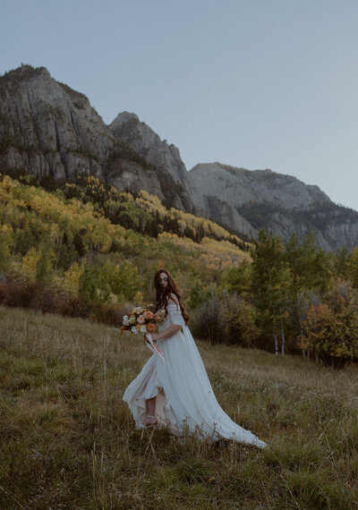 Bride walks through Colorado mountains holding bouquet