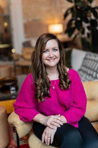 Bryony Williams in dark pink sweater sitting on a sofa