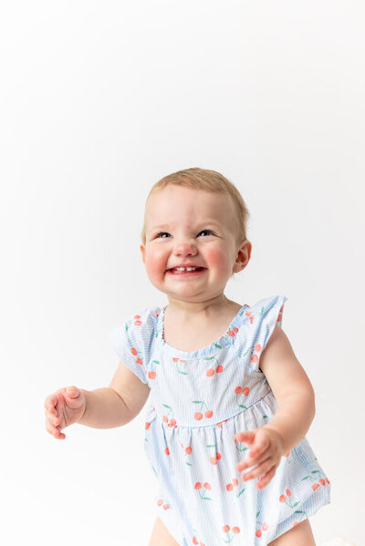 One year old girl dressed in blue laughs at camera.