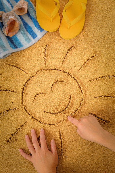 A child draws a smiling sun in the sand near the beach, symbolizing play, creativity, and the warm, supportive approach of Pacific Kids Occupational Therapy.