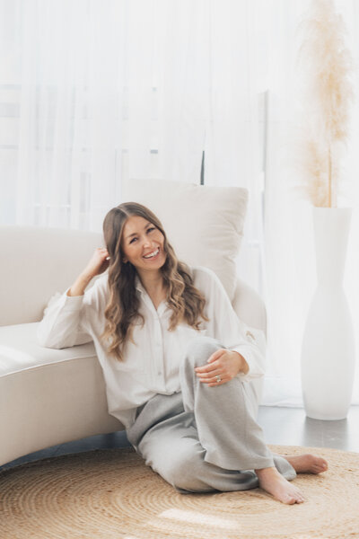 Justina Groff sitting cross-legged on the floor, working on a laptop in a bright, cozy living room