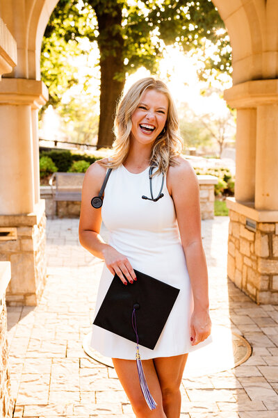 College graduation photos at the Trevecca University bell tower with the campus seal behind her, laughing and holding grad cap