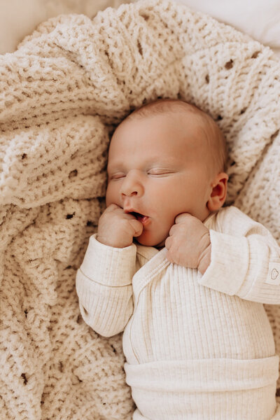 A newborn sleeping with his mouth open and his hand resting on his chin for a newborn family photoshoot.