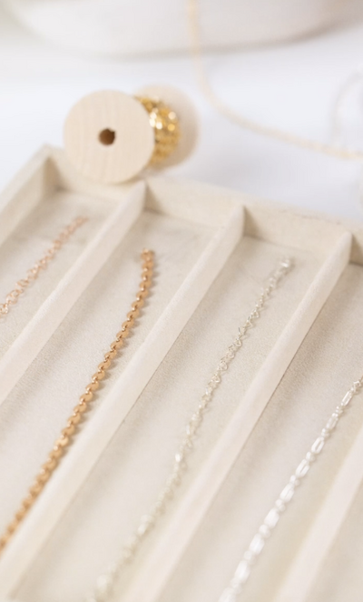 Close-up of gold and silver permanent jewelry chain options in display tray.