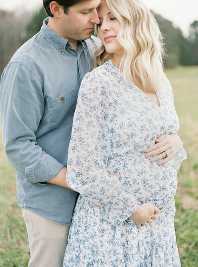 A couple embraces during their maternity shoot in a grassy field by Chattanooga photographer Kelsey Dawn Photography