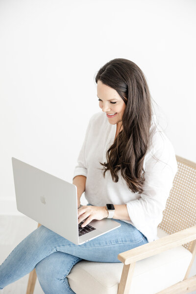 Kristin Wood sits and works on her laptop wearing a white blouse