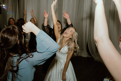 The wedding party and guests dance with the bride on the dance floor