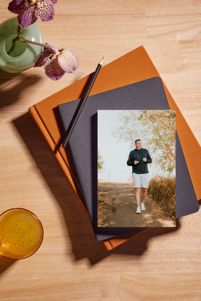 A stack of hardcover books with a framed pressed flower and dried leaves on a wooden table, styled with cozy, natural elements for a lifestyle aesthetic.