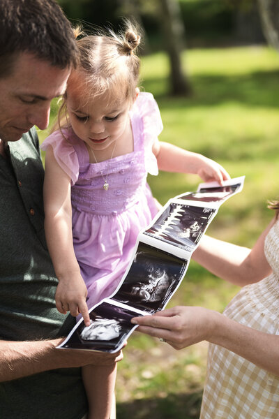 Photo of a man holding his daughter looking at an ultrasound picture.