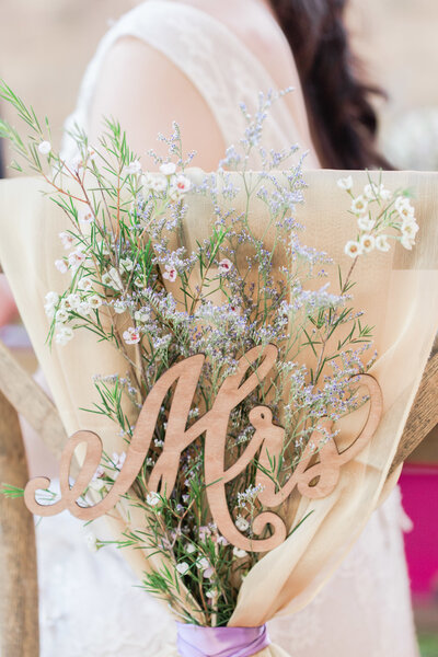 A wedding magazine surrounded by a Canon camera, red and pink cloth, flowers, leaves and a wedding ring