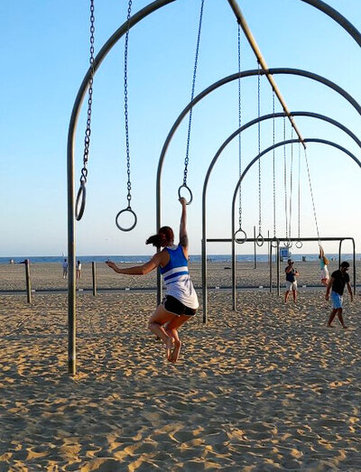 a woman swings from rings on the beach show show the benefits of having a fitness accountability group