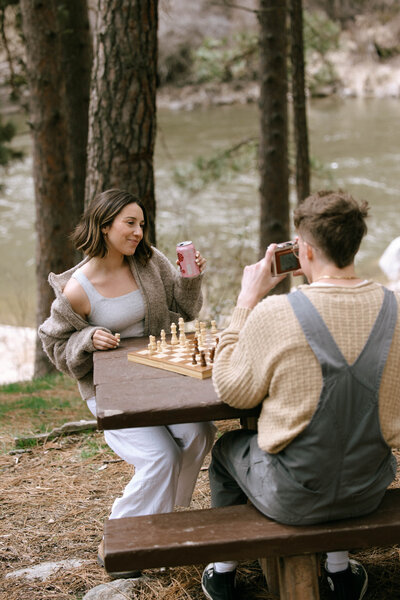 Couple enjoying a relaxed lifestyle photo session playing chess by a riverside picnic table in the Idaho mountains