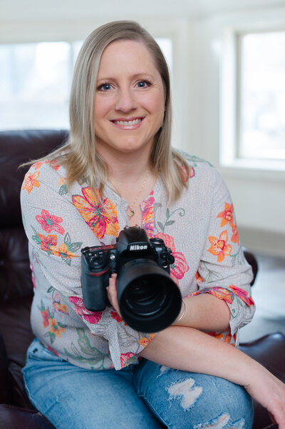 Creative Headshot of photographer Kristin Palkoner holding Nikon D3 camera and smiling.