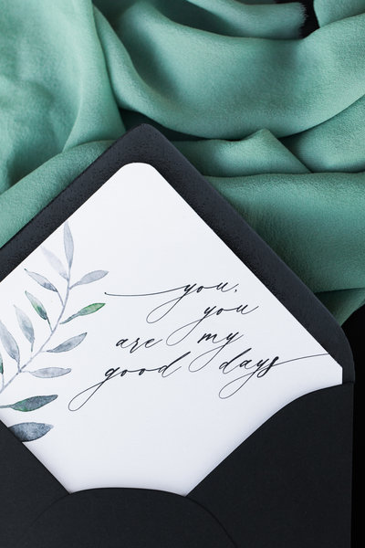 A wedding invitation with calligraphy rests on green fabric.