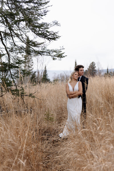 Adventurous elopement near a wooded shoreline, with wind moving through tall prairie grass and water glistening in the background.