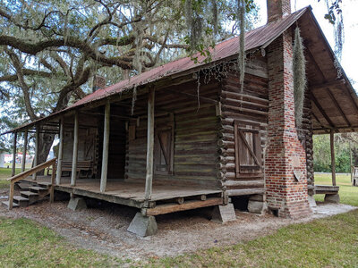 Nestled in a rustic setting, this historic log cabin with a wooden porch and partial brick chimney offers a serene escape. Surrounded by moss-covered trees, it's the perfect retreat for nature lovers exploring Mayo Florida campgrounds or enjoying camping adventures nearby.