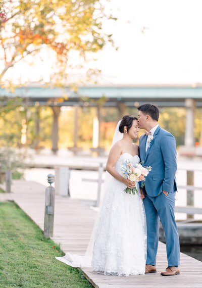 Groom kissing bride's forehead by the water at Harbour View in Woodbridge, Virginia. Captured by DC Wedding Photographer Bethany Aubre Photography.