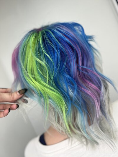 Image of client with hair that has been dyed bright green and blue with pink, purple, and grey highlights.