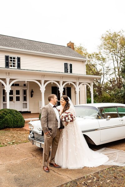 Groom in tweed suit with bride in front of white vintage car at the Cool Springs House
