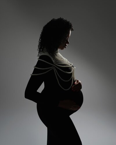 Studio maternity photo of a pregnant woman wearing layered pearl necklaces – available at Hello Photography Austin