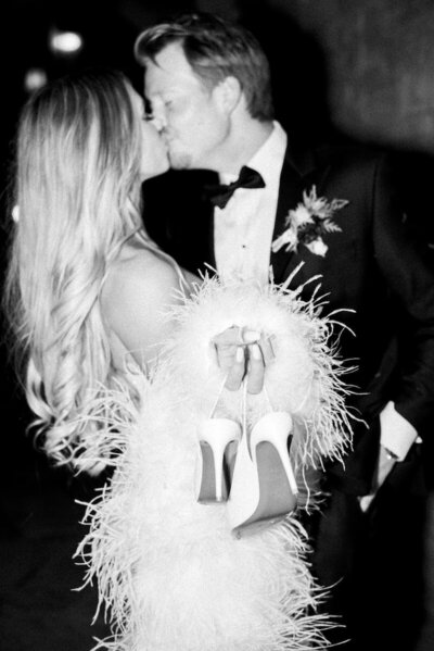 Black and White photo of couple kissing while holding Louis Vuitton wedding shoes