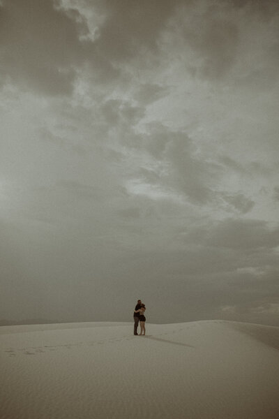 Couple embracing each other at the sand dunes under a cloudy sky.