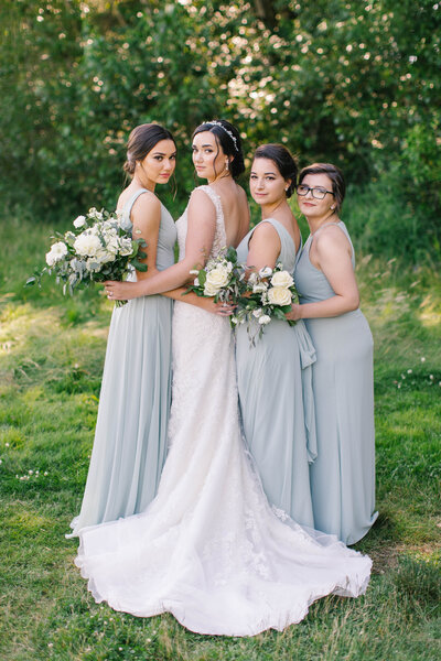 Bride and her bridesmaids in light blue dresses looking back over their shoulders with their arms around each other