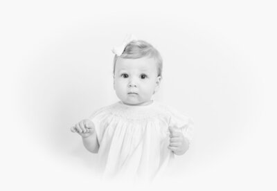Black-and-white heirloom portrait of a baby girl in a smocked dress with a bow in her hair.
