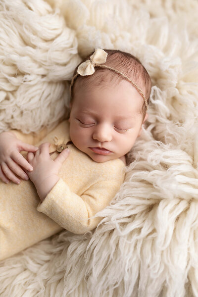 Newborn baby girl wrapped in tiffany blue fabric wearing a matching bow headband during her newborn photography session.