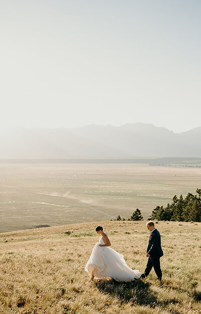 jackson hole photographers photographs bride and groom walking together with the bride walking in front of her groom while holding her gown for a candid wedding photo for a wyoming elopement