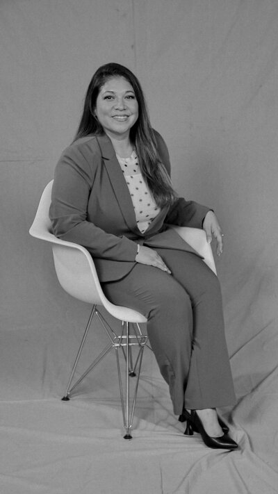 Teresa Cordoba is wearing a pantsuit, with polka dotted blouse, while smiling and sitting professionally in a chair.