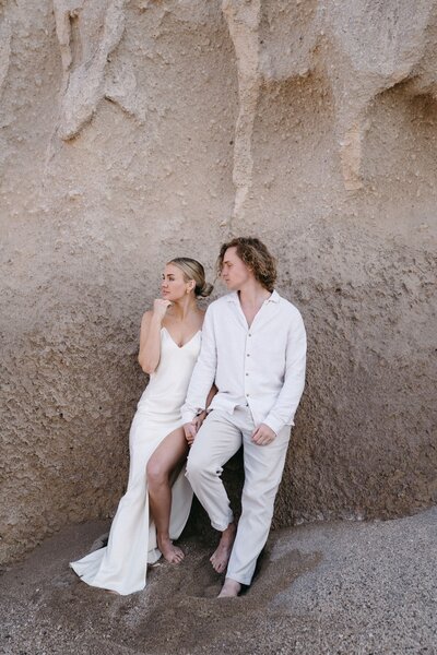 Bride and groom in all white on beach rocks