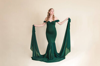 A pregnant woman in a green dress posing in a studio in Gainesville, VA.
