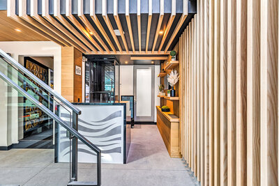 A hotel lobby with wooden panels across wall and ceiling. Front desk with beach waves on it and wooden shevles to the right of it with greenery as decor.